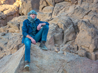Man in a keffiyeh sitting on a rock in the desert