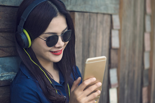 Happy Asian Woman Listening To Music On Her Headphone And Watching Movie Clip On Her Smart Phone