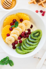 Healthy breakfast: fresh cottage cheese with orange,banana, kiwi, cranberry and honey on white wooden table. Selective focus