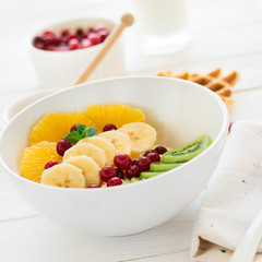Healthy breakfast: fresh cottage cheese with orange,banana, kiwi, cranberry and honey on white wooden table. Selective focus