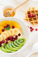 Healthy breakfast: fresh cottage cheese with orange,banana, kiwi, cranberry and honey on white wooden table. Selective focus
