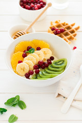 Healthy breakfast: fresh cottage cheese with orange,banana, kiwi, cranberry and honey on white wooden table. Selective focus