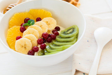 Healthy breakfast: fresh cottage cheese with orange,banana, kiwi, cranberry and honey on white wooden table. Selective focus
