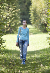 The young woman in a blue jacket walks in summer park.