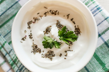 Greek yogurt with basil and parsley. White wooden background.
Top view.