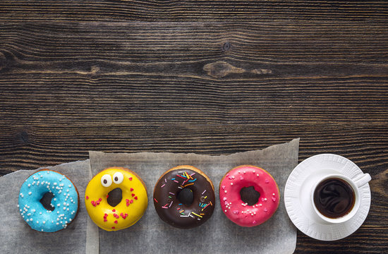 Multi-colored donuts with a cup of coffee on a wooden table. Copy space.