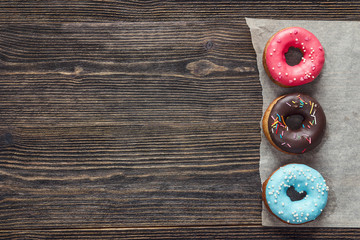 Multi-colored donuts with frosting on a dark wooden background. Space for text.