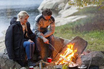 Couple Sitting By Campfire On Lakeshore