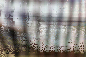 Metal mesh screen on window with rain water drops in squares