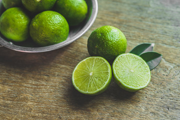 Fresh limes in a bowl with leaves cut in half on wooden table, Top view, background.