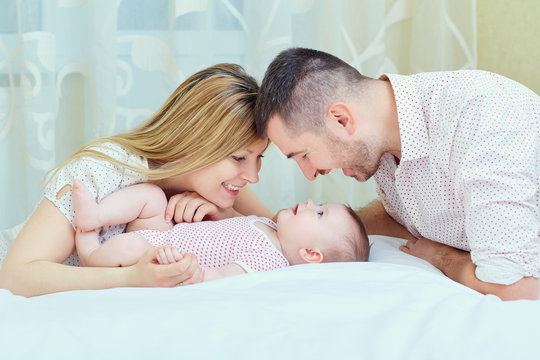 Mother and father playing with baby on the bed. A happy family.