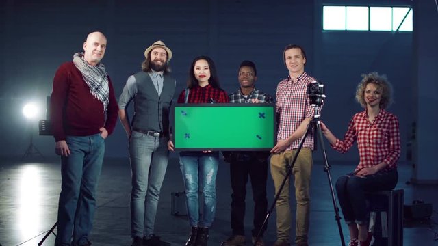 Cheerful film diverse team posing with a chromakey board.