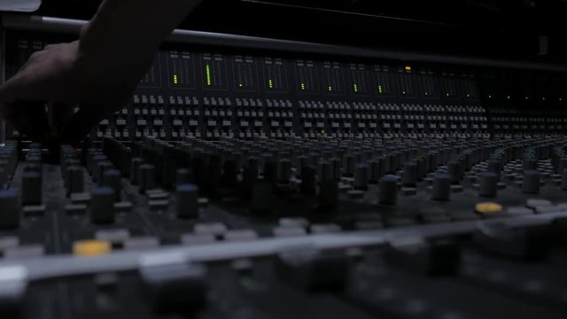 A Music Producer Tweaking Knobs on A Professional Analog Audio Mixer in a Studio