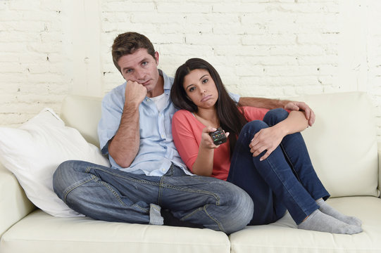 couple watching television together at home sofa couch looking bored frustrated switching channels