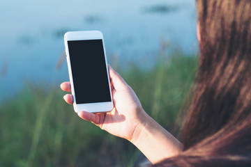 Mockup image of a woman using smart phone with blank black screen at outdoor and lake nature background
