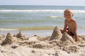 Boy sitting next to sand castle