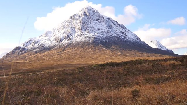 Sunny winter day on meadow at river Coupall at delta to river Etive. Snowy cone of mountain Stob Dearg 1021 metres high. Higland in Scotland an marvelous day. Dry grass and heather bushes on banks. 