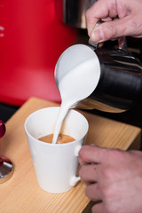 Barista filling up cappuccino with milk froth