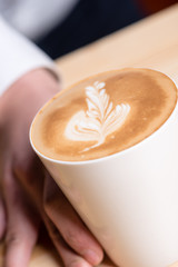 Waiter handing over cappuccino with leaf drawn into milk froth, selective focus