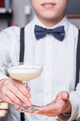 Bartender handing over cocktail with both hands, with foam, pale dogwood pink, selective focus