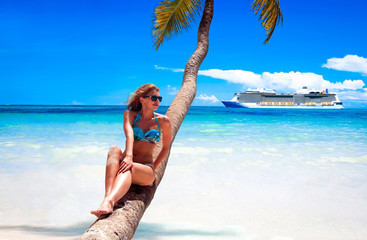 Cruise vacation concept. Cruise ship in the sea near the tropical island with woman sitting on a coconut palm tree near the sea. Relaxing and enjoying vacation.