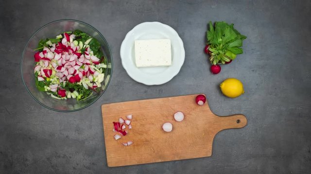 Preparing fresh vegetable salad with greek cheese. Top view on grey kitchen counter with ingredients and accessories. Food stop motion animation.