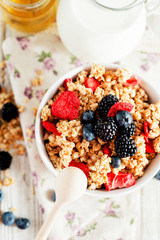 
healthy and hearty breakfast of muesli , oatmeal or granola with berries , blackberries , blueberries and strawberries , honey , milk and green tea on a wooden background