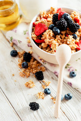 
healthy and hearty breakfast of muesli , oatmeal or granola with berries , blackberries , blueberries and strawberries , honey , milk and green tea on a wooden background