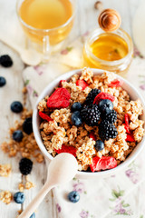 
healthy and hearty breakfast of muesli , oatmeal or granola with berries , blackberries , blueberries and strawberries , honey , milk and green tea on a wooden background