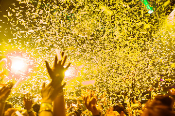 Confetti fired in the air during a in a disco. Hundreds of hands to the sky. Yellow tone/background
