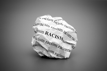 Crumpled paper ball with words Racism on gray background