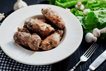 charcuterie, meat, baked pork rolls with mushrooms, herbs and lettuce on a wooden black background 