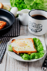 a delicious and hearty breakfast, fried eggs in a white toast with spices, peppers, lettuce, a cup of black coffee and milk on a wooden background 