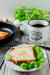 a delicious and hearty breakfast, fried eggs in a white toast with spices, peppers, lettuce, a cup of black coffee and milk on a wooden background 