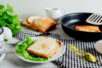 a delicious and hearty breakfast, fried eggs in a white toast with spices, peppers, lettuce, a cup of black coffee and milk on a wooden background 