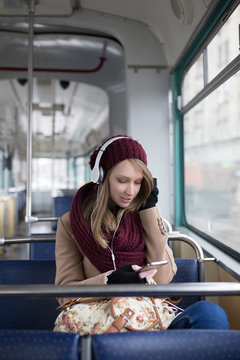 Beautiful young woman sitting in tram, listening to music and looking through window. 