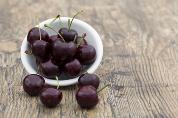 Close-up of cherries in a white bowl on brown background