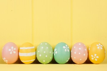 Row of hand painted Easter eggs over a yellow wooden background