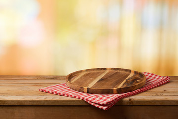 Wooden cutting board with checked tablecloth on table over blurred bokeh background