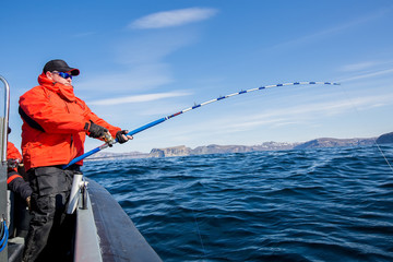 Man pulls out of Sea fish. Spinning bend. Red Jacket. sports glasses. fisherman