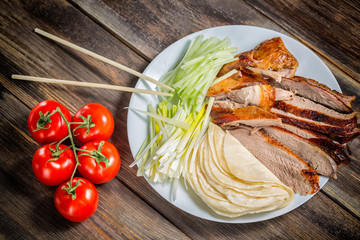 Beijing chinese Duck meat served with onions, pancakes, cucumber pieces and tomatoes on white plate with chopsticks close up. Wooden table and top view