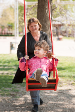 Grandmother Pushing Granddaughter On Swing In Park