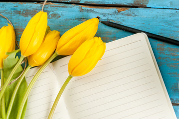Flowers yellow tulips and notebook for notes or wishing on blue rustic table top view, copy space, for Valentine's, Mothers day or Women's day