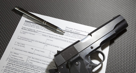 Semi-auto handgun with a pen on top of the FBI paperwork for a background check required to legally purchase it, the 4473