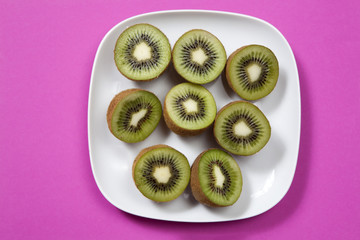 the half kiwi fruit in a plate on a burgundy background as an art work that can be used for decoration