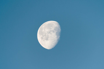 Waning moon in blue sky in early morning, showing detailed craters