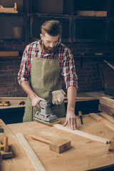 Handsome young man with glasses and hairstyle has serious hobby. Cabinetry grinds wooden plank at his workstation