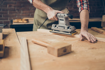 closeup photo of cabinetmaker grinds wooden plank on tabletop at workstation