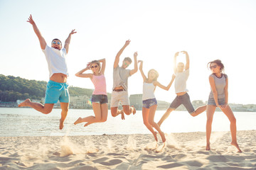 Group of happy young cheerful students jumping on the beach