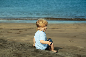 Cute baby boy sits on sand on sandy beach